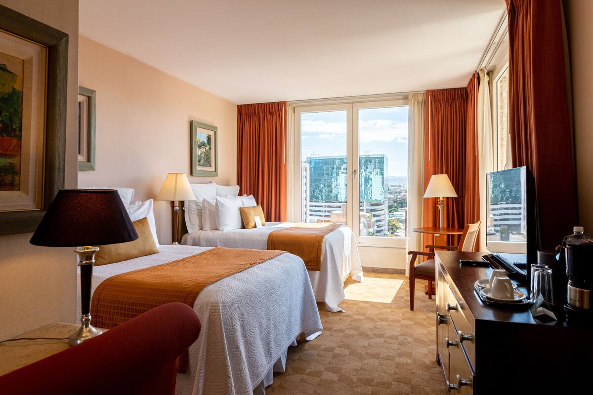 A hotel room with two beds, a desk with a coffee maker, and a view of the city.