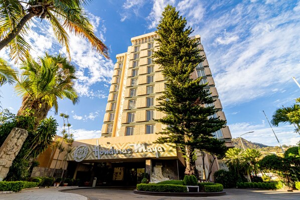 Un hôtel doté d’une façade moderne, d’une entrée imposante et entouré de verdure.