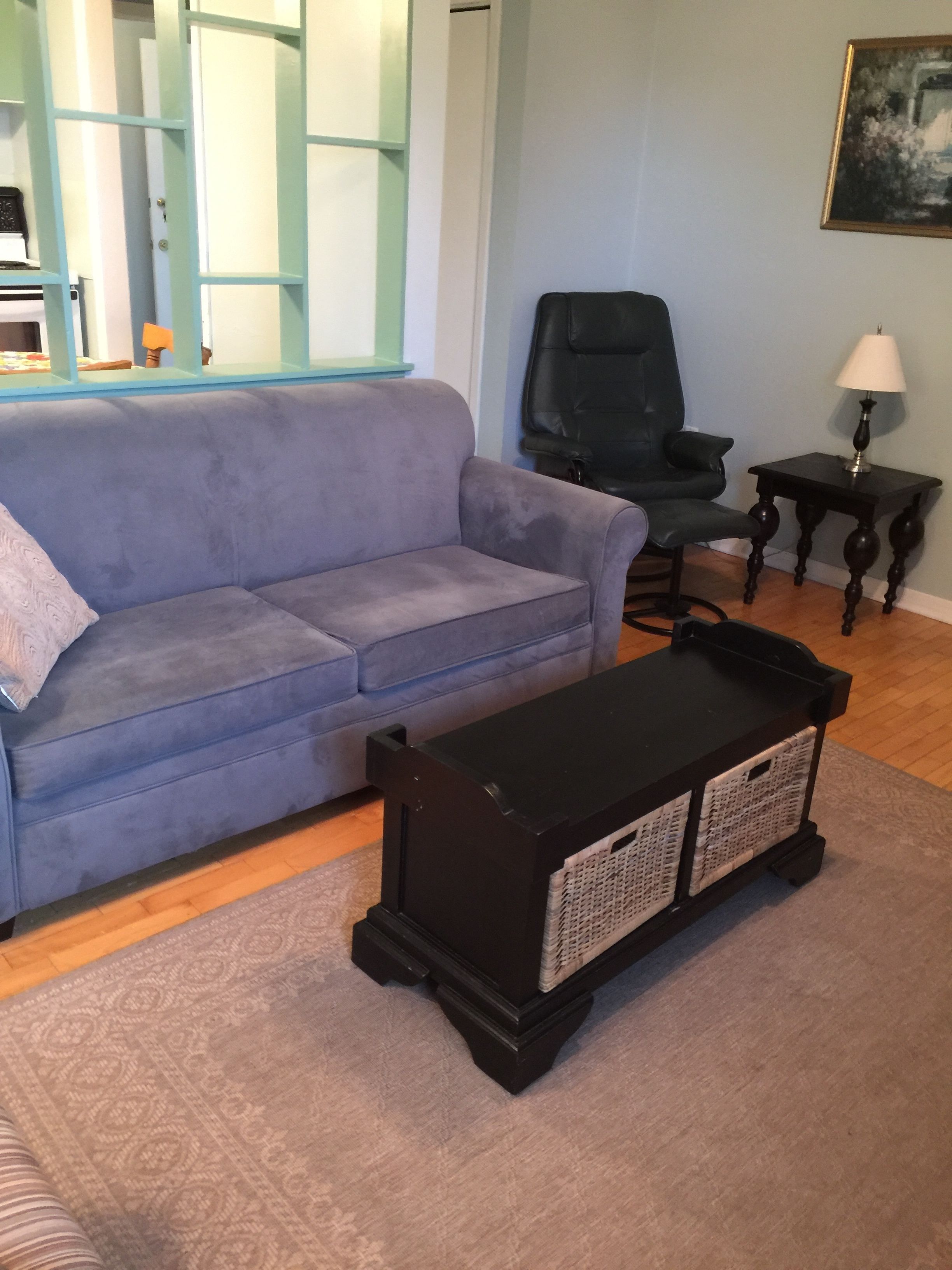 A living room with a blue sofa, a black coffee table, a black chair, and a small table with a lamp.