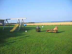 A grassy field with a swing set, a lantern, and a small table with objects. - Dreamweavers Cottages and Vacation Homes (North Rustico)