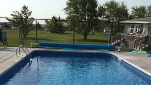 A clear swimming pool with a blue interior, surrounded by a fence and a grassy area.