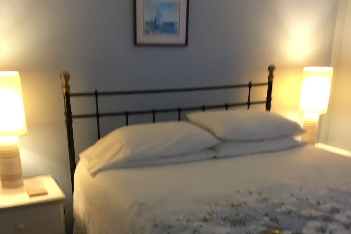 A bedroom with a bed, two bedside lamps, a nightstand, and a framed picture on the wall.