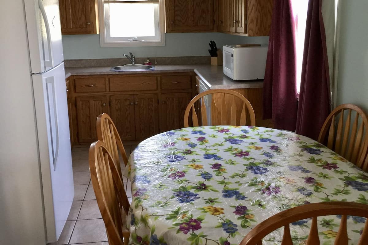 A kitchen with wooden cabinets, a white refrigerator, a microwave, a sink, and a dining table with chairs.