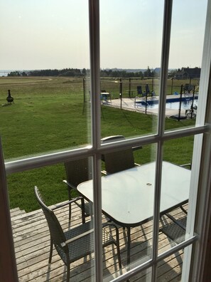 A view from a window overlooking a grassy area with a pool and outdoor furniture. - Dreamweavers Cottages and Vacation Homes (North Rustico)