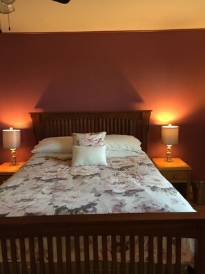 Un lit avec une couvre-lit à motifs floraux, deux lampes de chevet et une tête de lit en bois.
