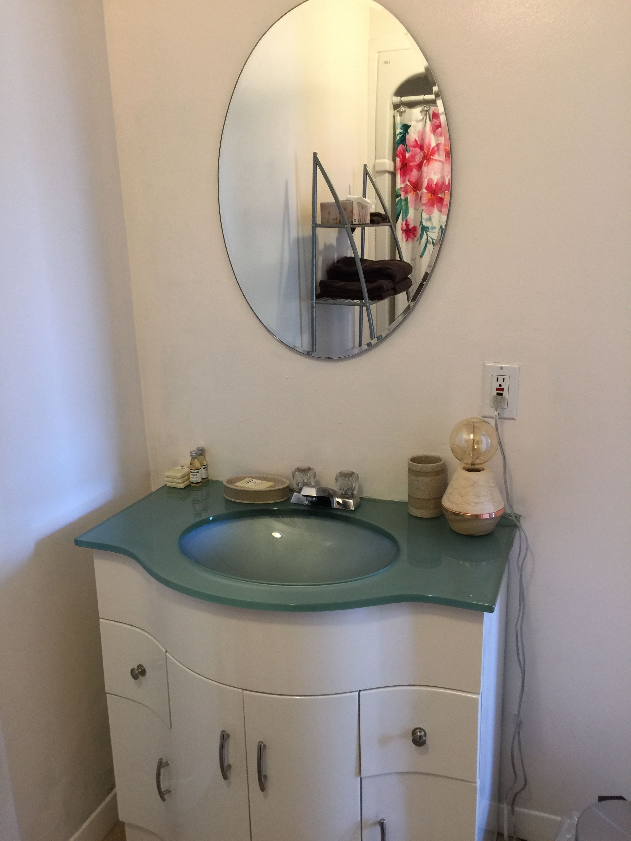 A bathroom with a round mirror, a green sink, and a white cabinet with drawers.
