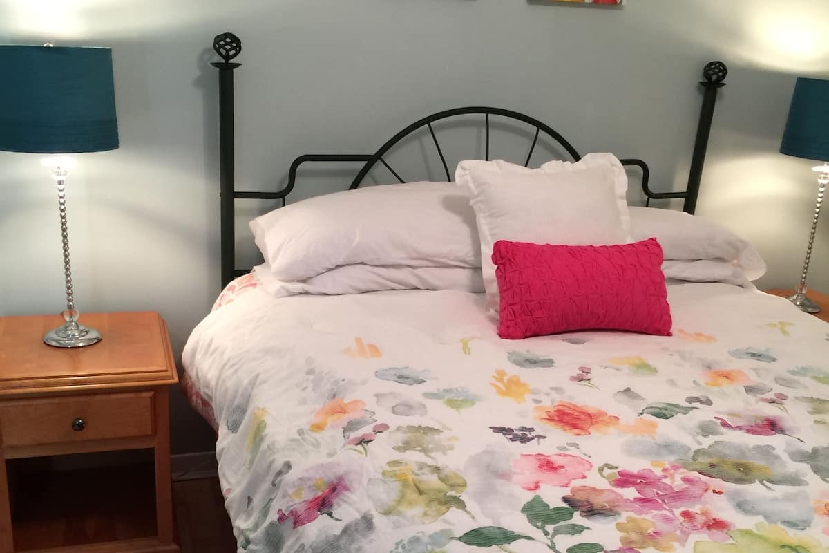 A bedroom with a bed, two bedside tables, a nightstand, and two wall-mounted lamps.
