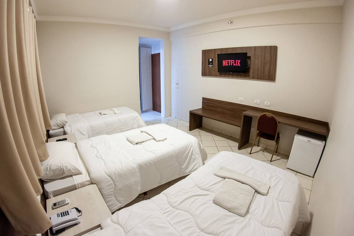 Ein Hotelzimmer mit drei Betten, einem Schreibtisch, einem Fernseher und einem kleinen Kühlschrank.