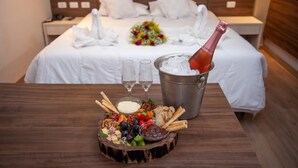 A neatly made bed with white linens, a bouquet of flowers, and a bottle of champagne in a bucket. - London Hotel (Londrina)