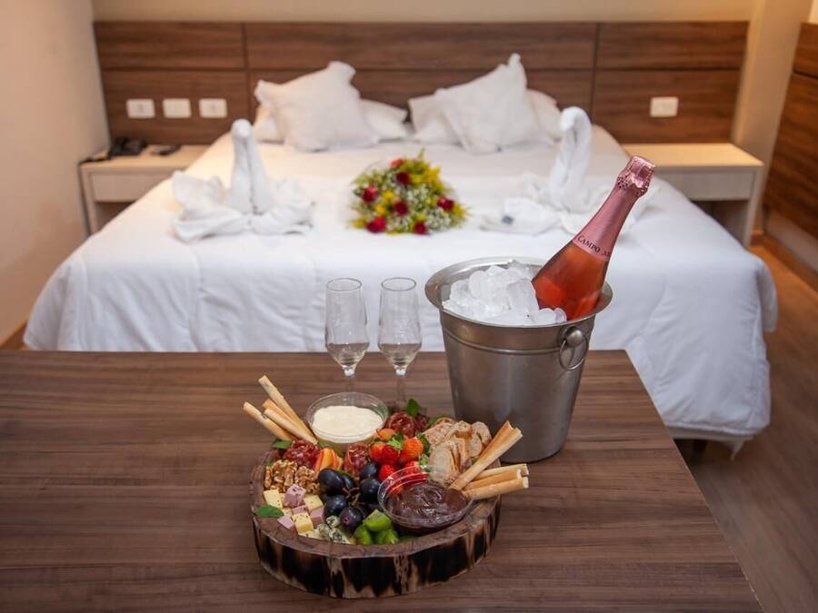 A neatly made bed with white linens, a bouquet of flowers, and a bottle of champagne in a bucket.