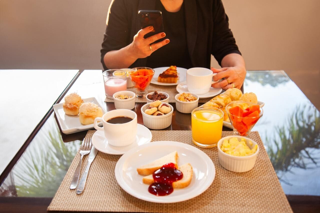 Et morgenbord med forskellig mad og en person, der bruger en smartphone.