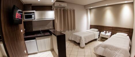 A compact hotel room with a kitchenette, two single beds, a TV, and a shower area.