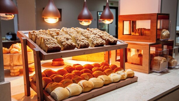 A bakery display with various baked goods, including bread and pastries, under warm lighting. - London Hotel (Londrina)