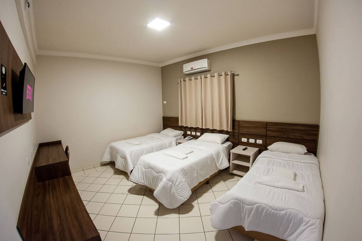 Ein Hotelzimmer mit zwei Einzelbetten, einem Holztisch, einem Nachttisch und einer Wandklimaanlage.