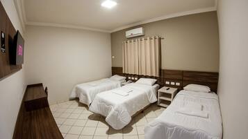 A hotel room with two single beds, a wooden desk, a nightstand, and a wall-mounted air conditioner.