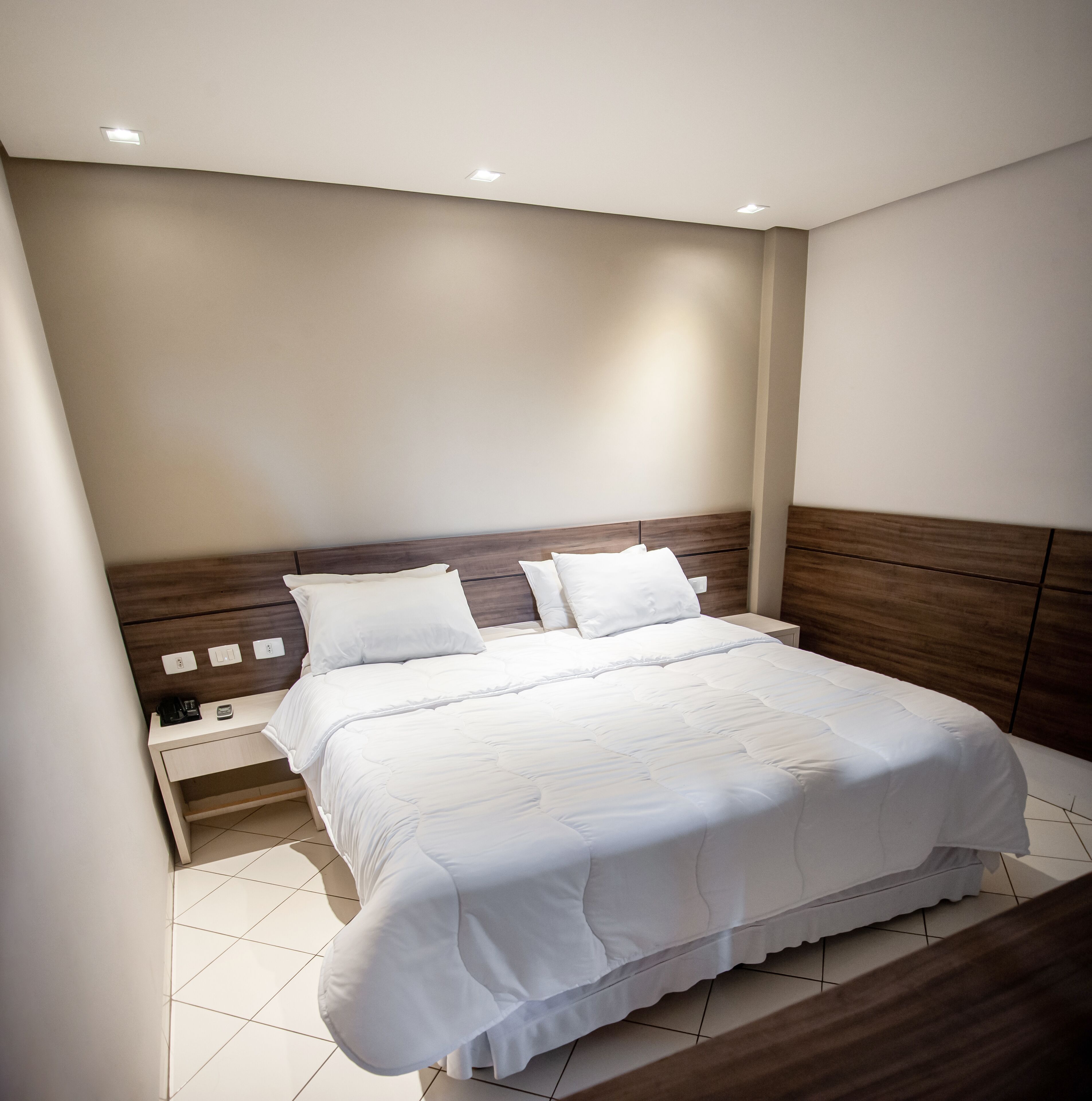 A neatly made bed with white bedding in a modern room with a wooden headboard and a nightstand.