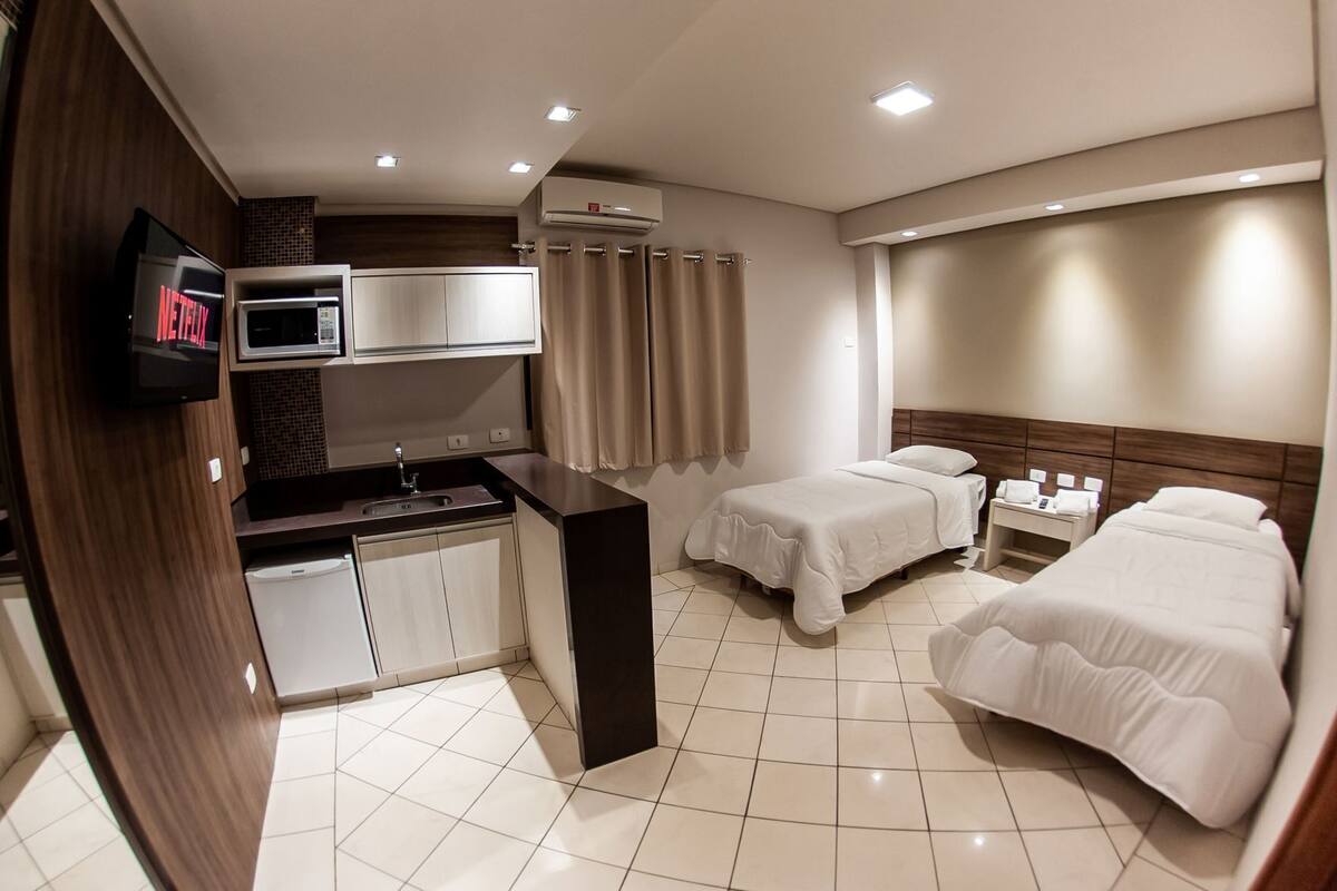Ein Hotelzimmer mit Küchenzeile, Fernseher, zwei Betten und einem Badezimmer.
