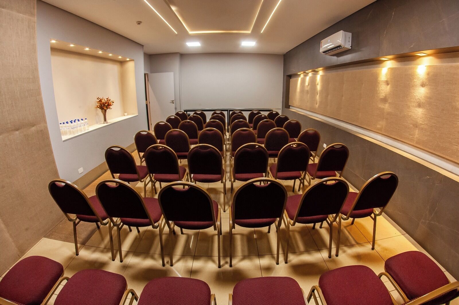 A conference room with rows of chairs facing a whiteboard, a small shelf with items, and an air conditioning unit on the wall.