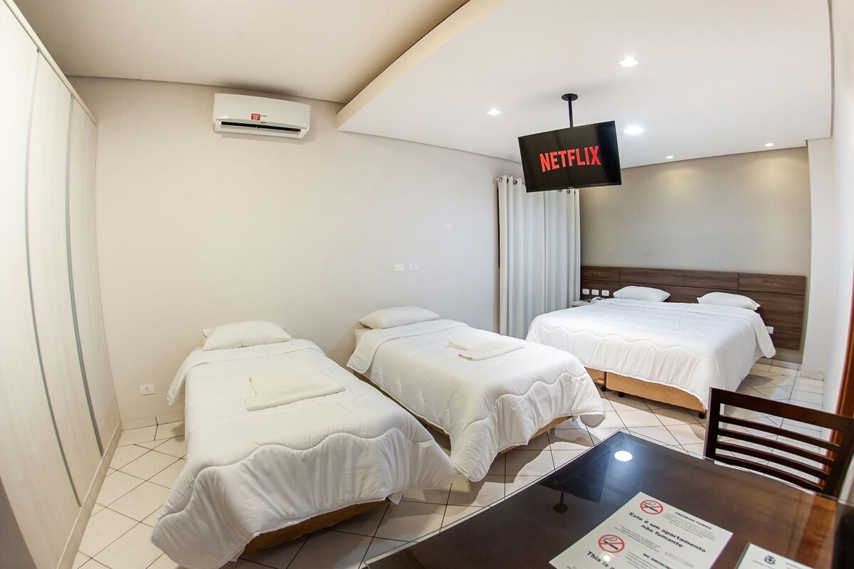 A hotel room with two single beds, a TV screen displaying 'NETFLIX,' a table with a menu, and a chair.