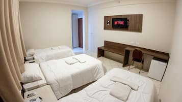 Une chambre d’hôtel avec trois lits, un téléviseur fixé au mur, un bureau et un petit réfrigérateur.