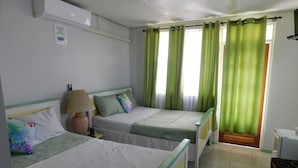 A hotel room with two single beds, a bedside table with a lamp, a green curtain, and a window with green curtains. - Mr. Clean Bed and Breakfast (Roseau)