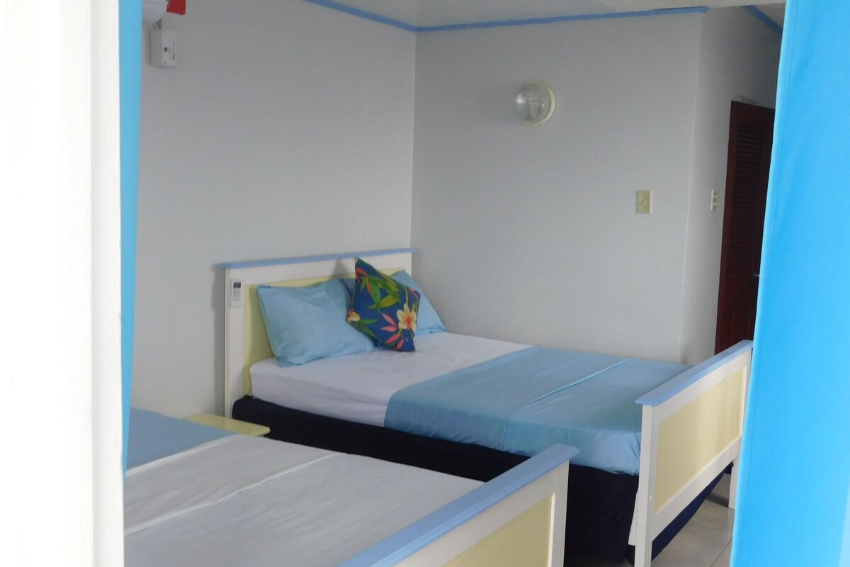 A single bed with a blue headboard and a colorful pillow in a room with white walls and a blue trim.