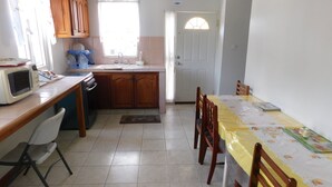 A compact kitchen with a microwave, stove, and sink. There is a dining table with chairs and a window with curtains. - Mr. Clean Bed and Breakfast (Roseau)