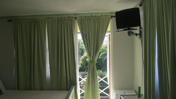 A room with a bed, a television mounted on the wall, and a window with curtains. - Mr. Clean Bed and Breakfast (Roseau)