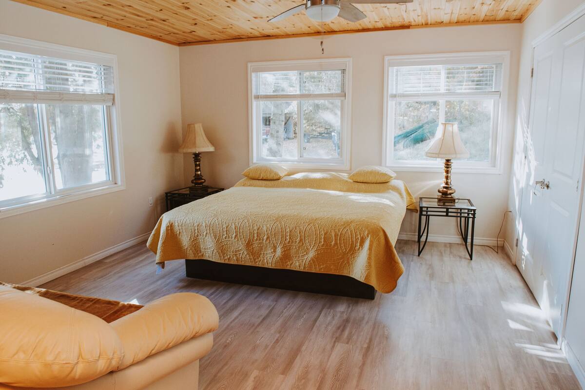 A bedroom with a bed, two bedside tables, a lamp, and large windows.