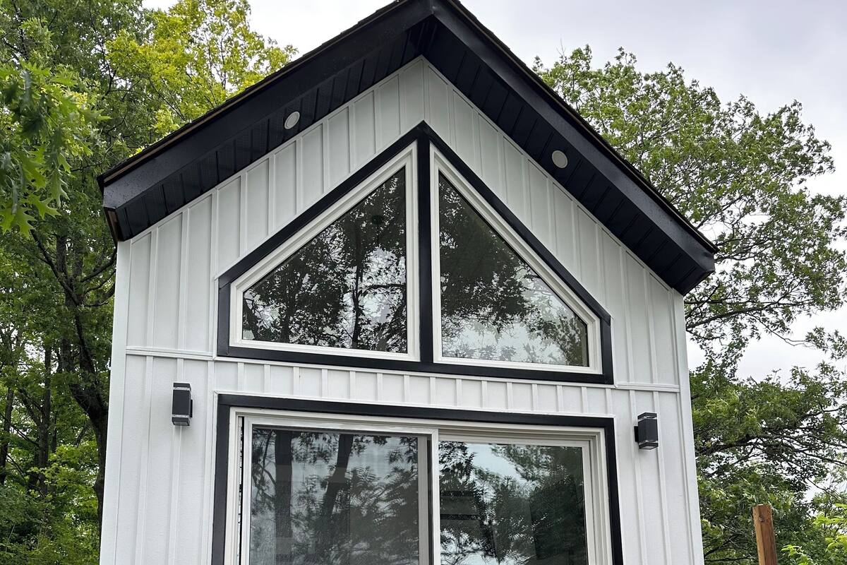 A two-story cabin with a steeply pitched roof, large windows, and a wooden staircase leading to the entrance.