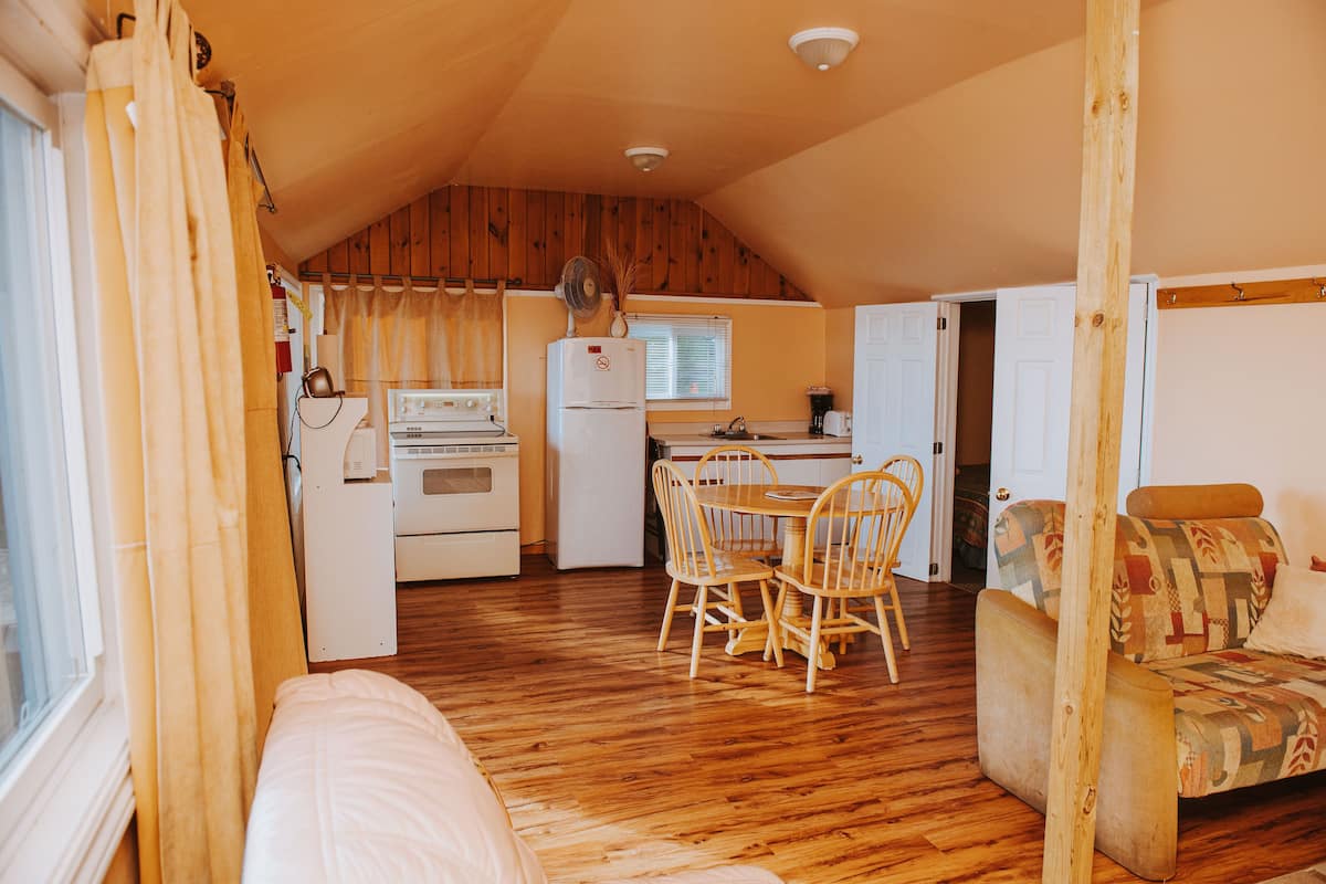 A compact kitchen with wooden cabinets, a refrigerator, and a dining area with a table and chairs.