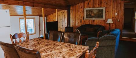 Una habitación con paneles de madera, una mesa de comedor, sillas, un sofá y un televisor.