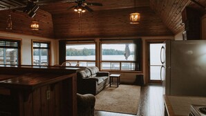 A cabin interior with a wooden ceiling, a sofa, a small table, and a refrigerator. - Lang Lake Resort (Unorganized North Sudbury)