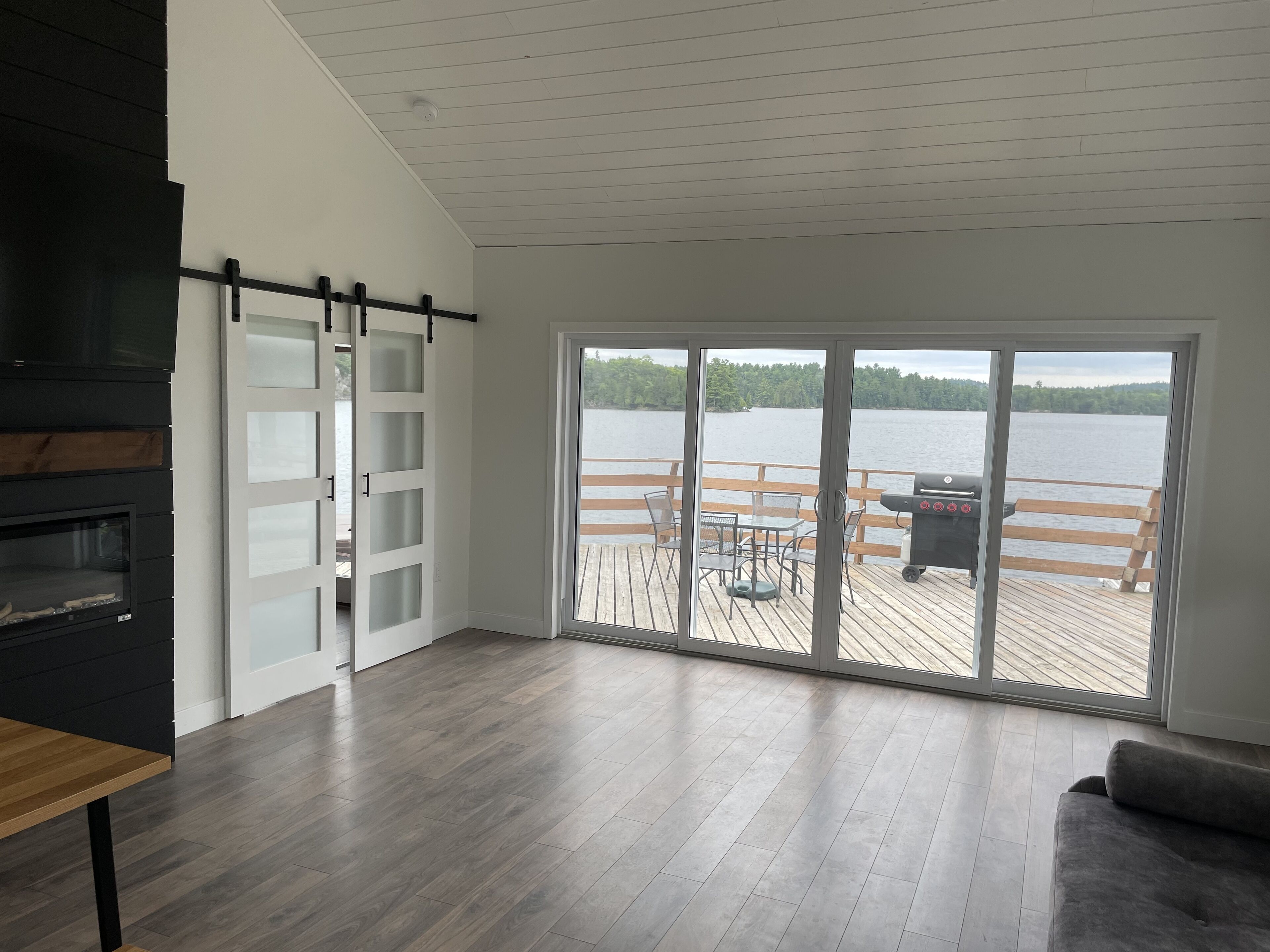 Una sala de estar moderna con un amplio ventanal corredero que da a una terraza con vistas a un lago.