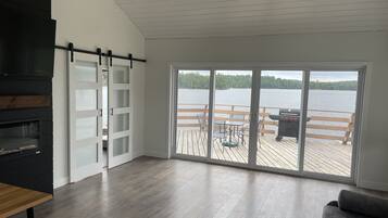 Una sala de estar moderna con un amplio ventanal corredero que da a una terraza con vistas a un lago.