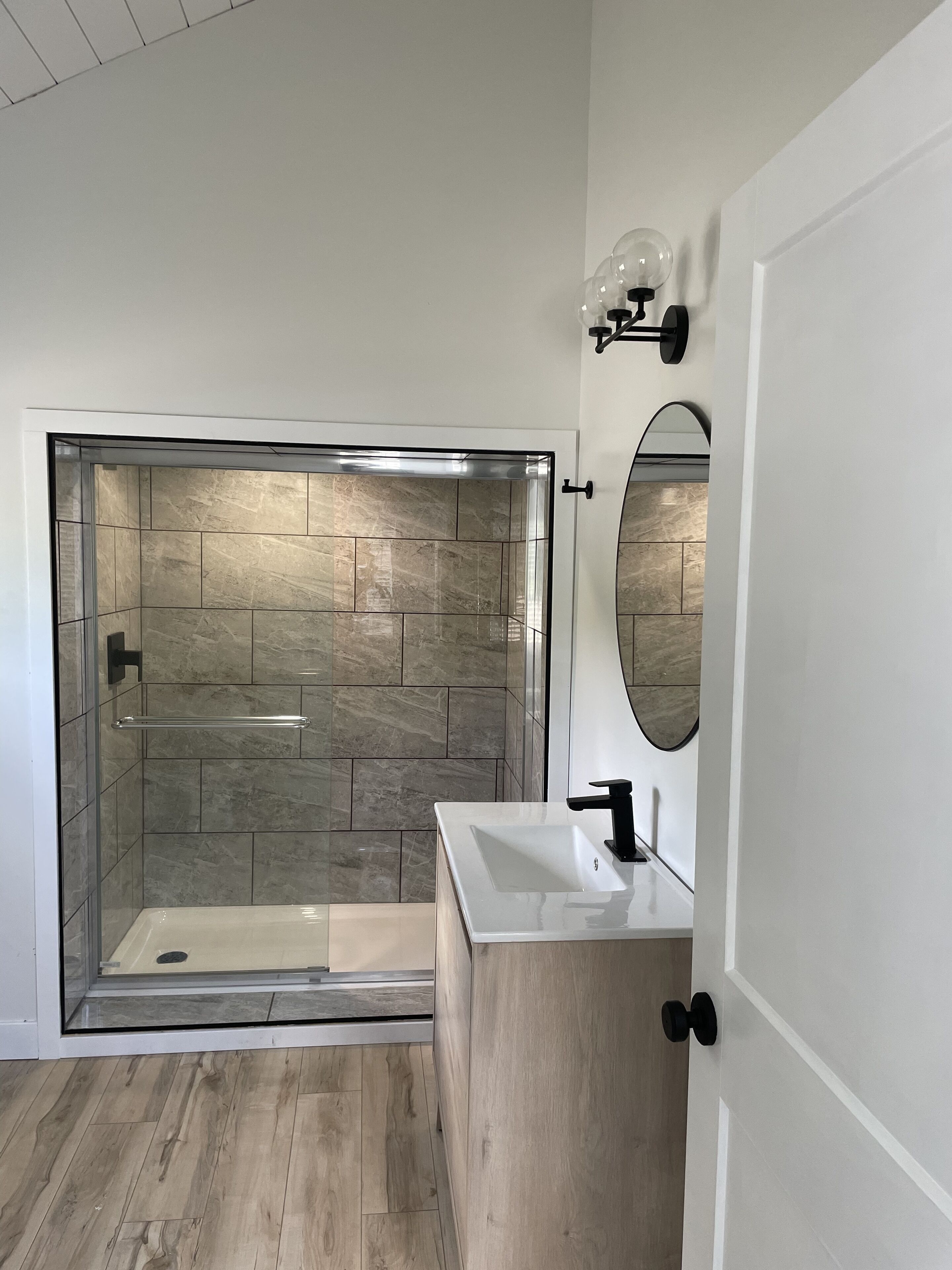 A modern bathroom with a glass-enclosed shower, a wooden vanity, and a mirror with wall-mounted lights.