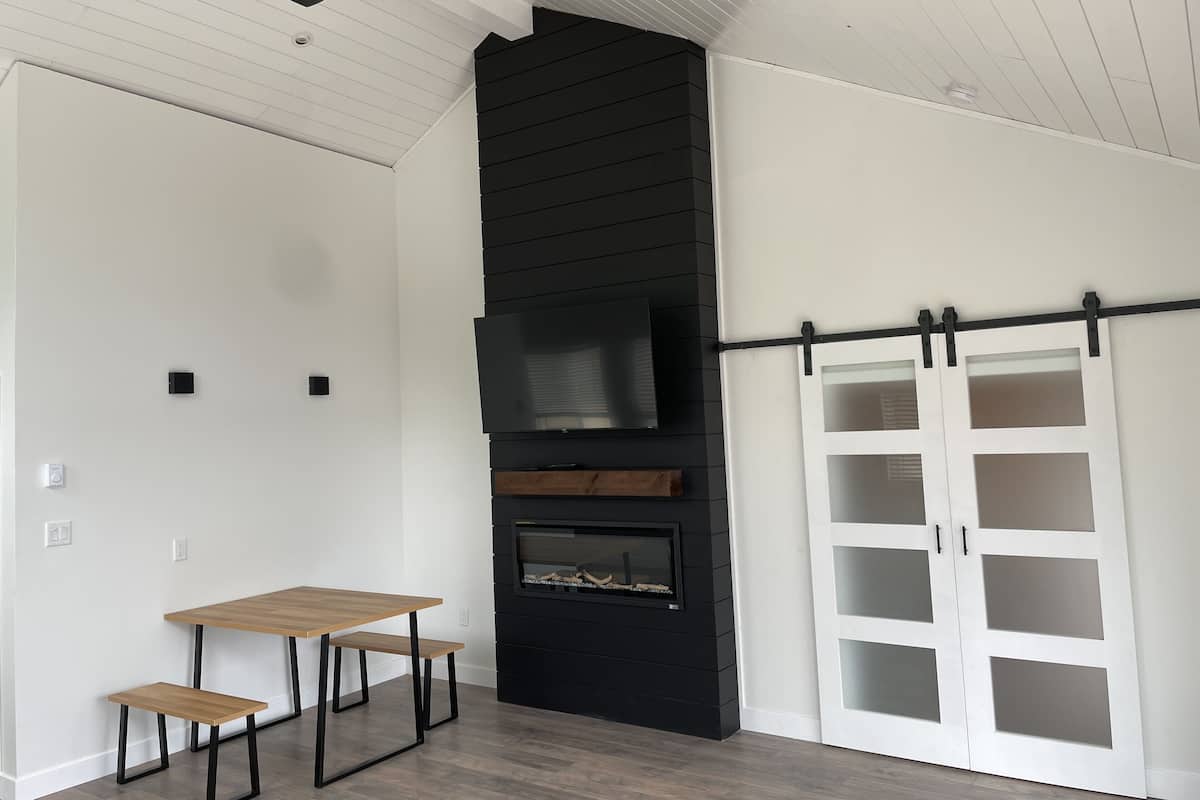 A modern interior with a wooden table and benches, a black fireplace, and a sliding white door.