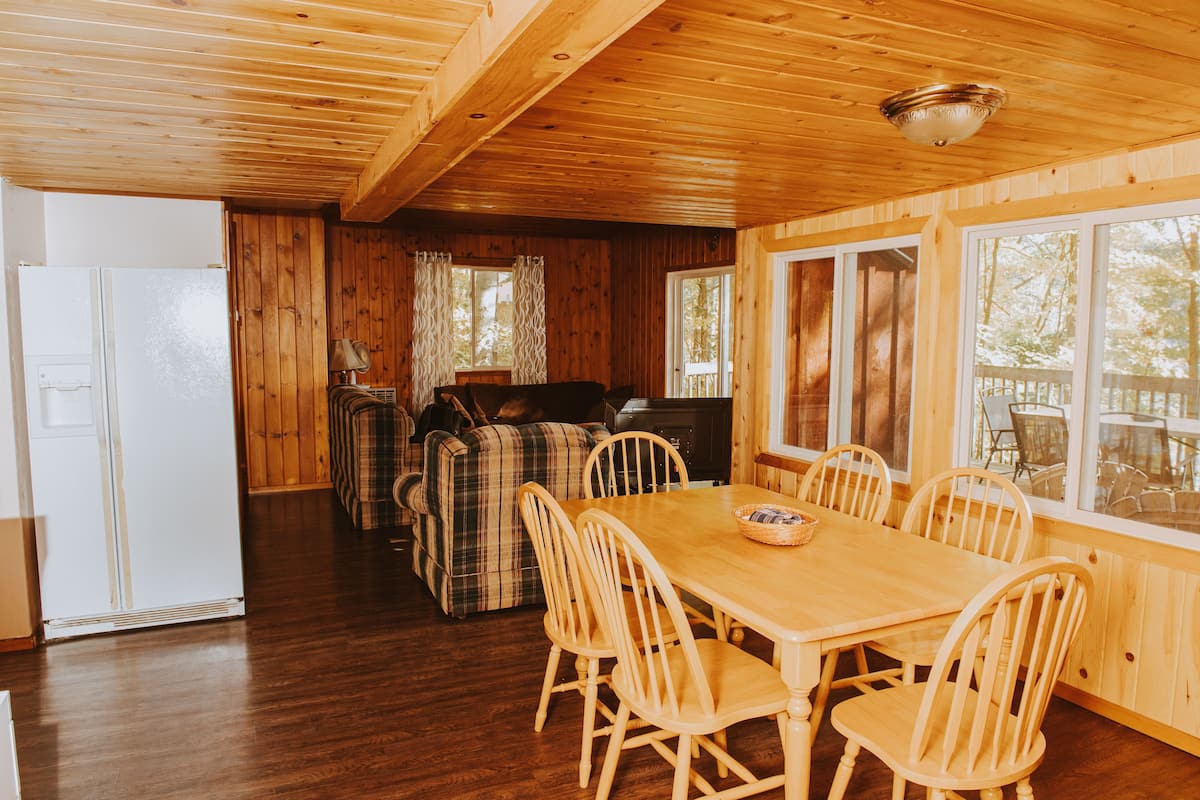A wooden interior with a dining table and chairs, a sofa, and a fireplace.