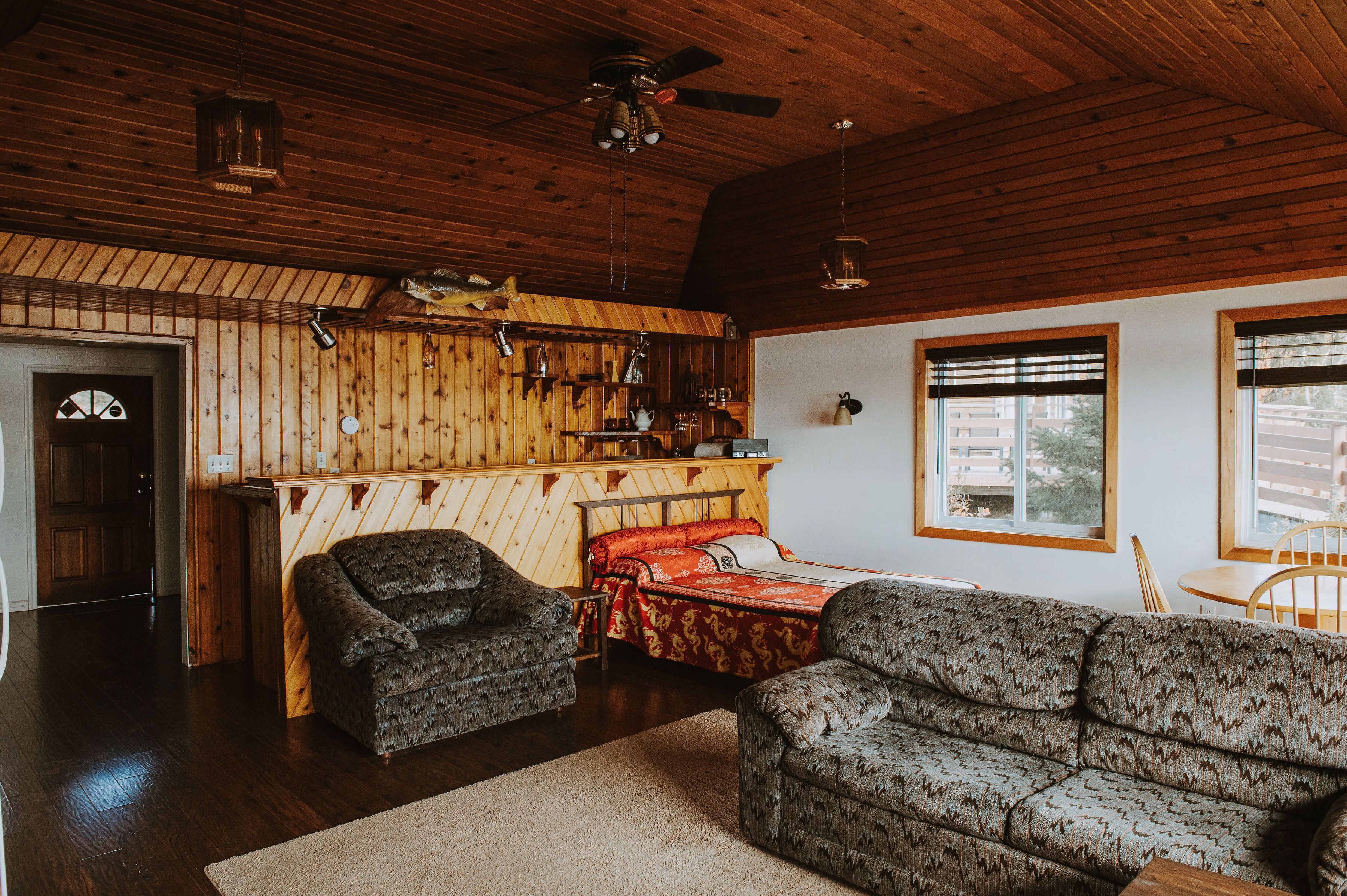 Une pièce chaleureuse avec un plafond en bois, un lit recouvert d’une courtepointe rouge et or, un canapé à motifs et une petite table.