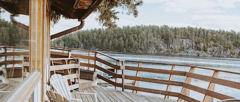 A wooden deck with chairs and a table, overlooking a body of water and forested area.