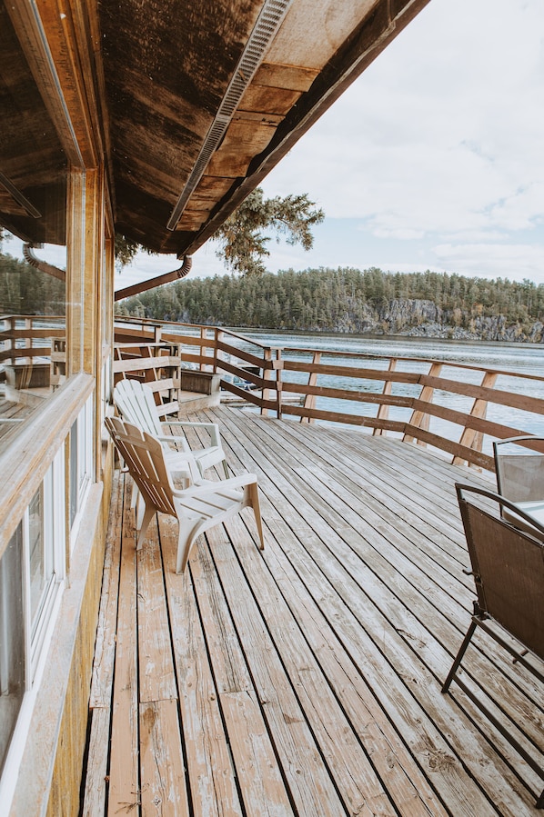 A wooden deck with chairs and a table, overlooking a body of water and forested area.