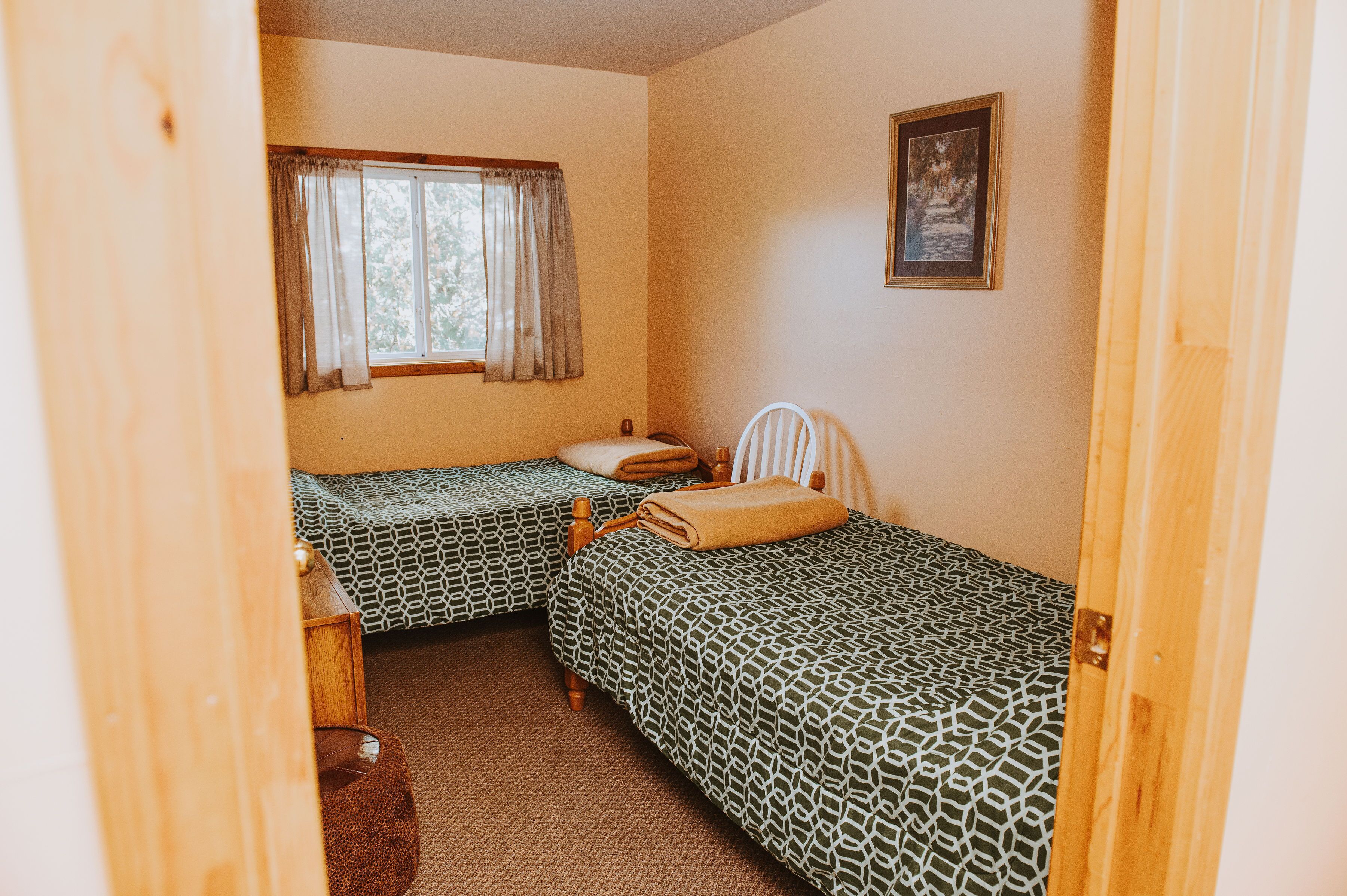 Una habitación con dos camas individuales, una mesita de noche de madera, una silla y una ventana con cortinas.
