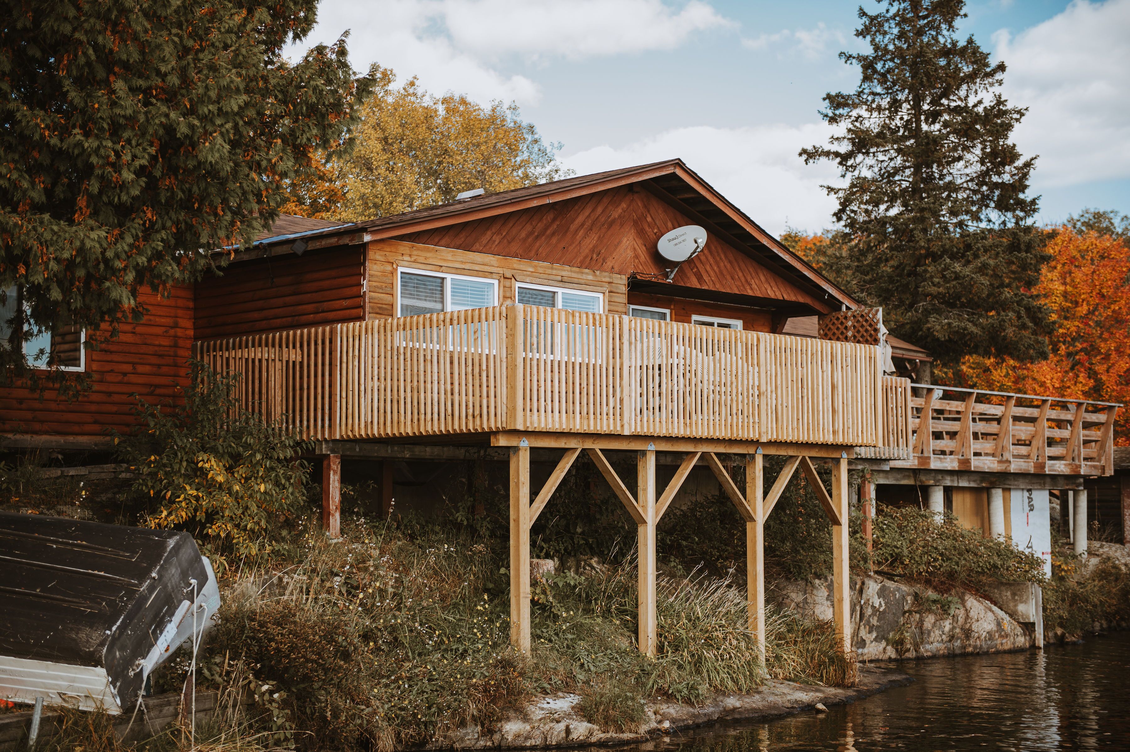 Une cabane en bois dotée d’une terrasse qui s’étend au-dessus de l’eau, entourée d’arbres et de végétation.