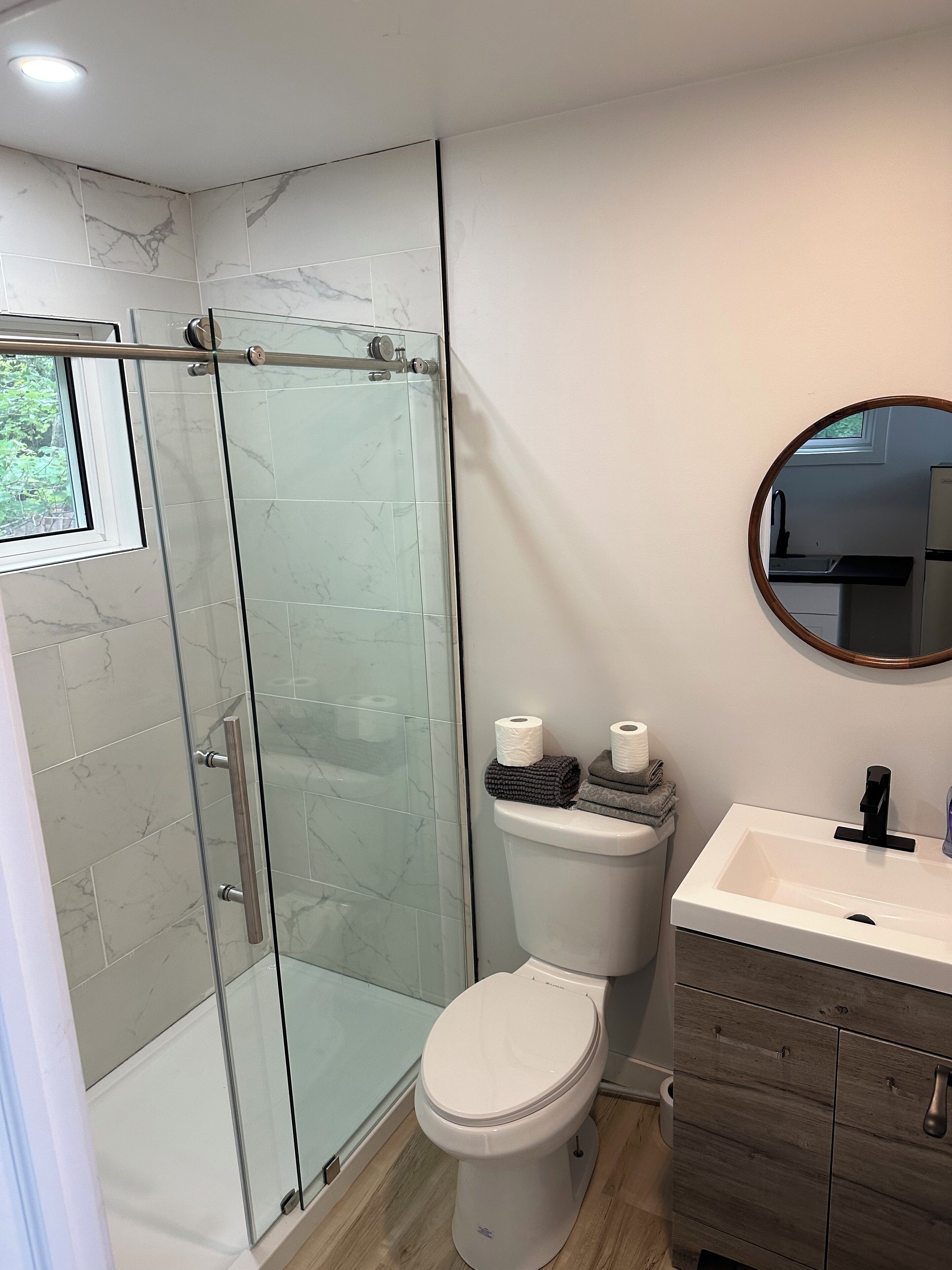 A modern bathroom with a glass-enclosed shower, a white toilet, and a wooden vanity with a sink.
