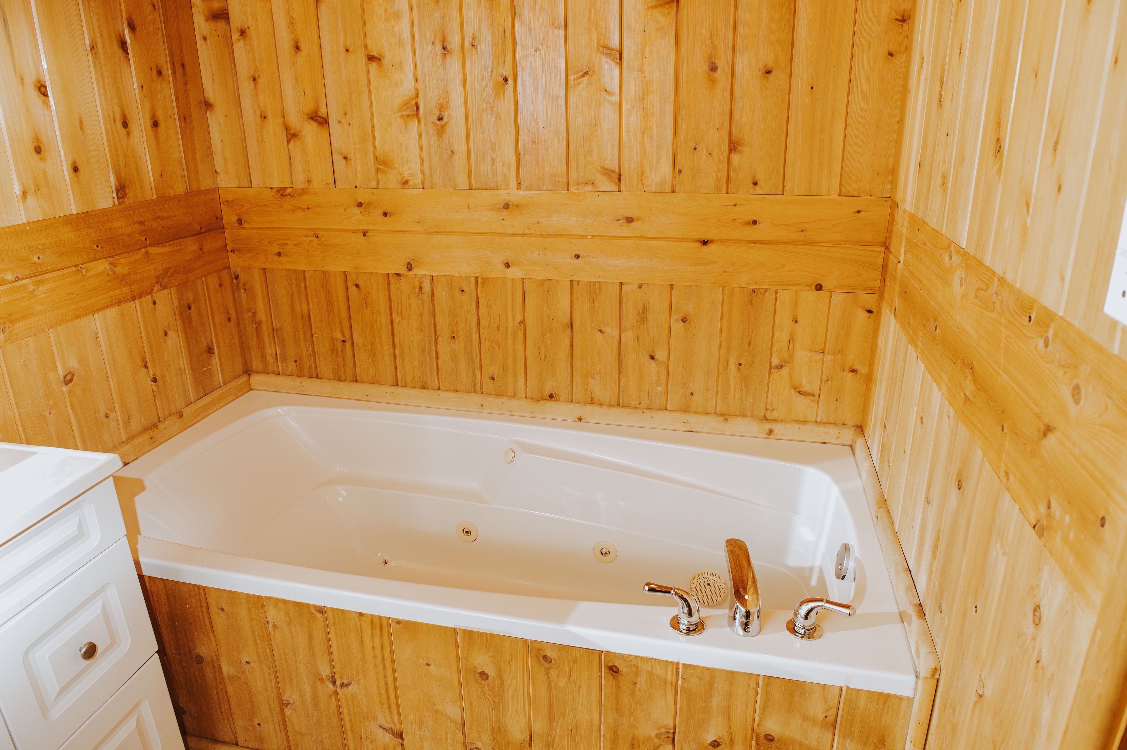 A wooden-paneled room with a white bathtub, wooden cabinets, and a wooden bench.