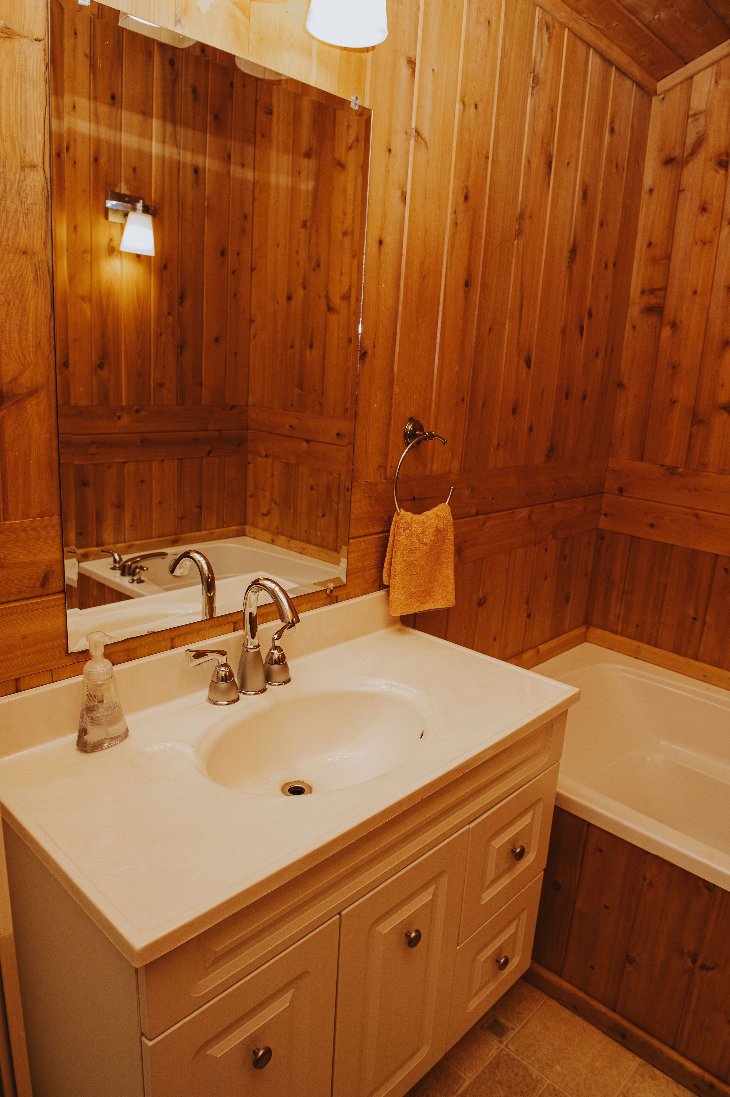 Une salle de bain aux murs lambrissés, avec un lavabo blanc, un miroir et une serviette accrochée au mur.