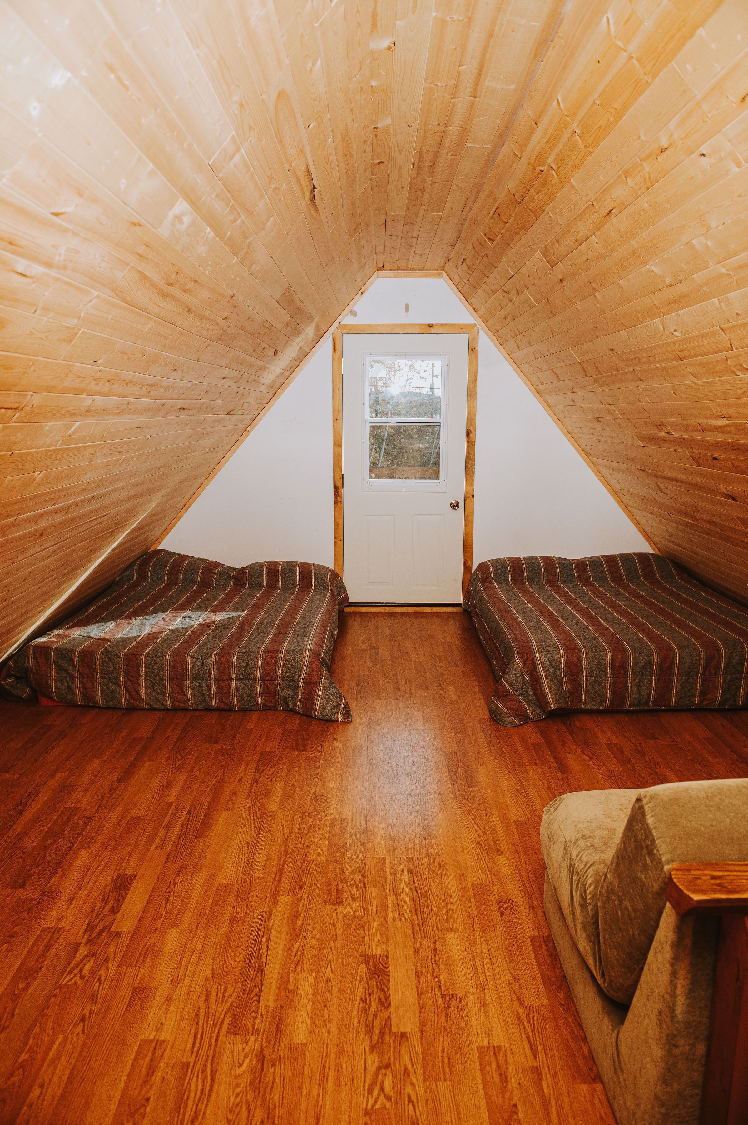 Um pequeno quarto no sótão com ripas de madeira no teto, chão de madeira e duas almofadas listradas no chão.