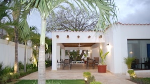 An outdoor patio with a covered seating area, palm trees, and potted plants. - Hotel Playa Catalina (La Romana)