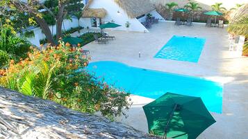 A swimming pool with a thatched-roof structure, lounge chairs, and a potted plant.