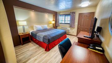 A hotel room with a bed, desk, chair, lamp, and a television.